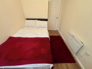 Una habitación pequeña y estrecha con una cama, una puerta y un radiador.