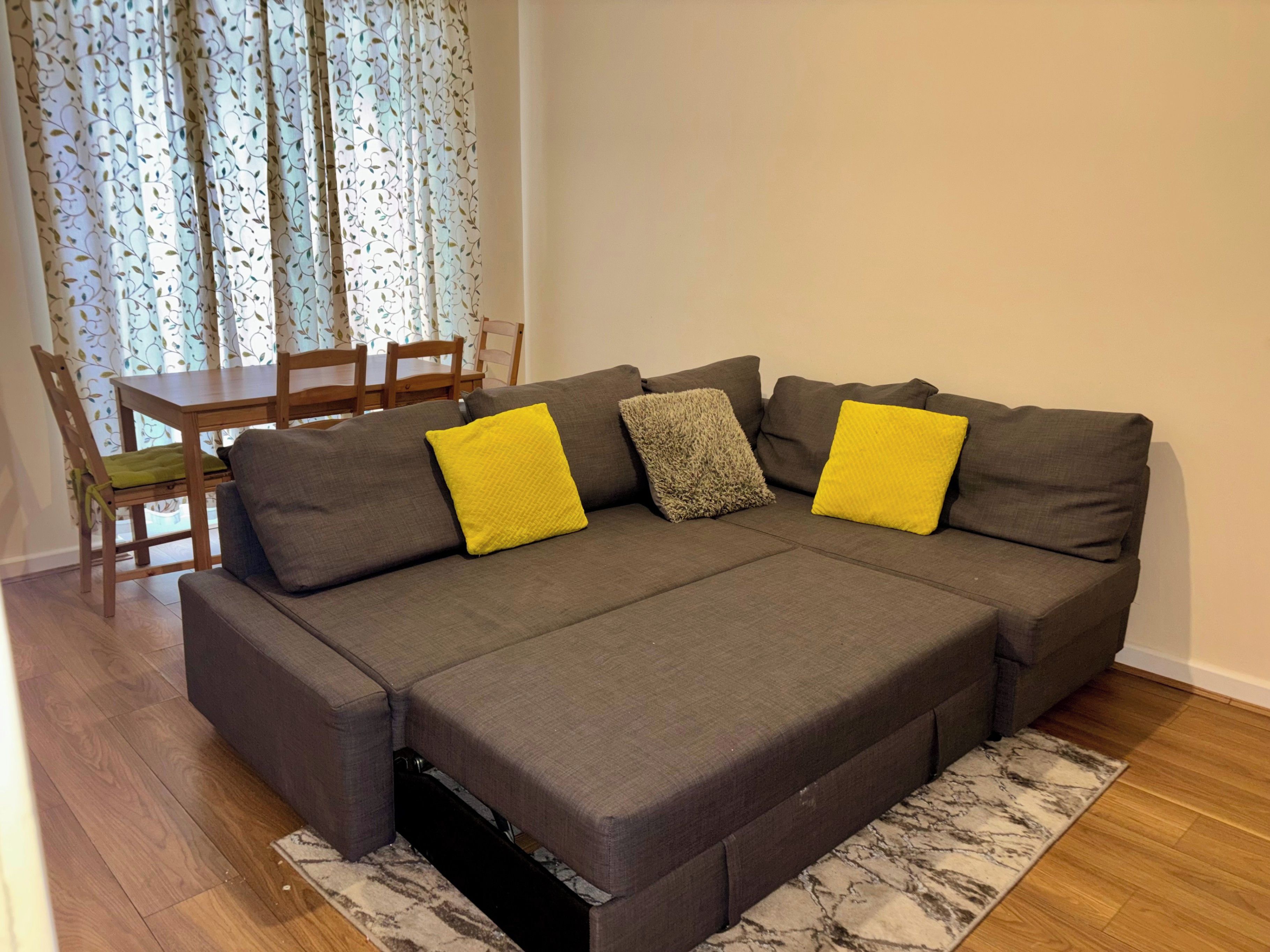 A sectional sofa with a pull-out bed, a dining table with chairs, and a patterned curtain.