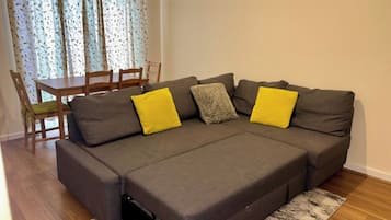 A sectional sofa with a pull-out bed, a dining table with chairs, and a patterned curtain.