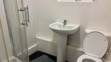 A bathroom with a glass shower enclosure, a white sink, and a toilet.