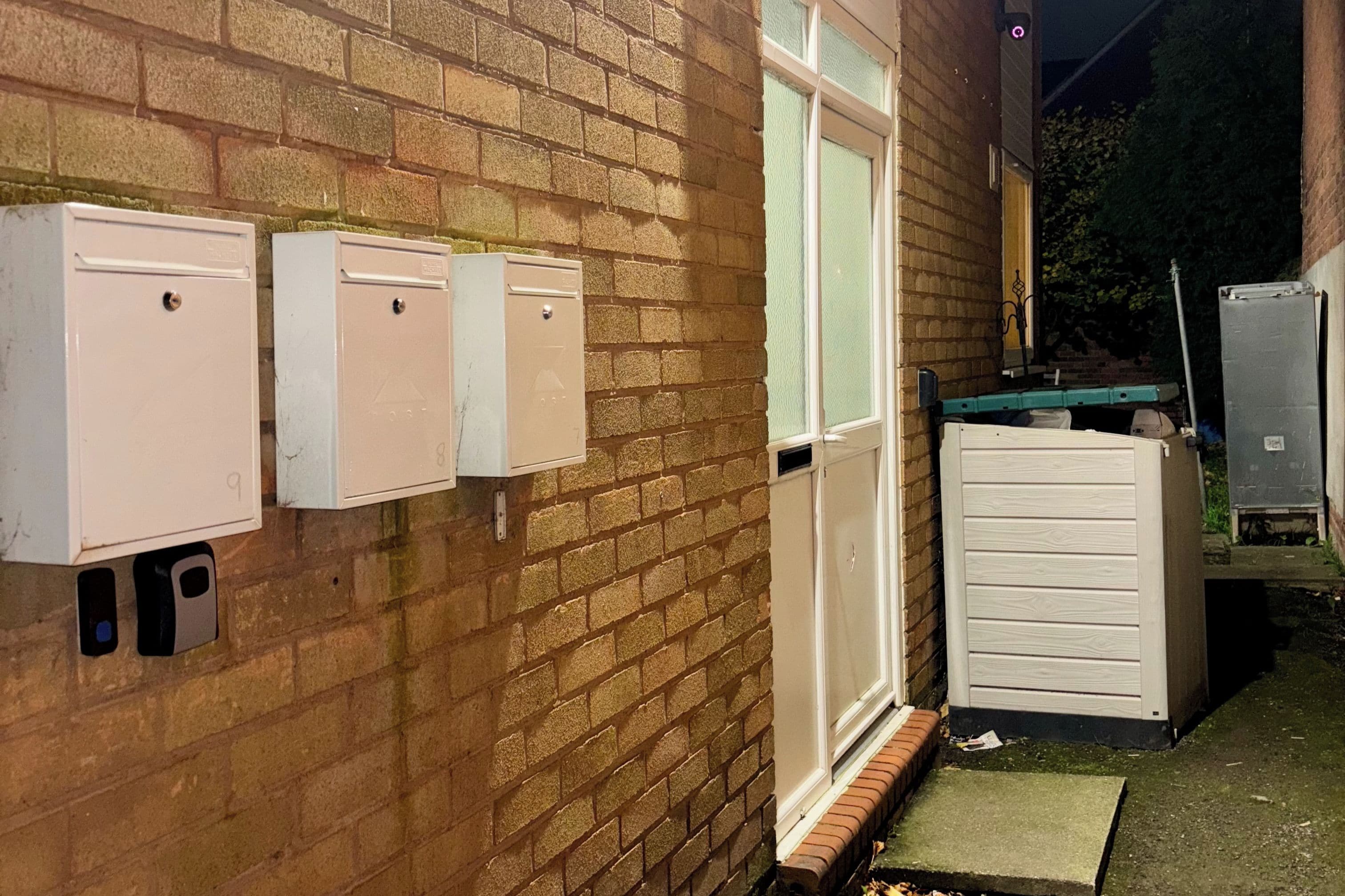 A brick building with three utility meters mounted on the wall and a white door.
