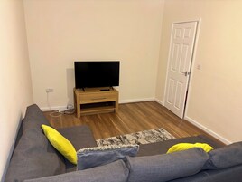 Un soggiorno con un divano grigio, una televisione su un mobile in legno e una porta sullo sfondo.