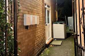 Un estrecho callejón con un muro de ladrillo, una puerta blanca y una reja de metal.