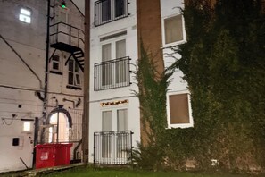 Un edificio con varias ventanas, un bote de basura rojo y un árbol en frente.