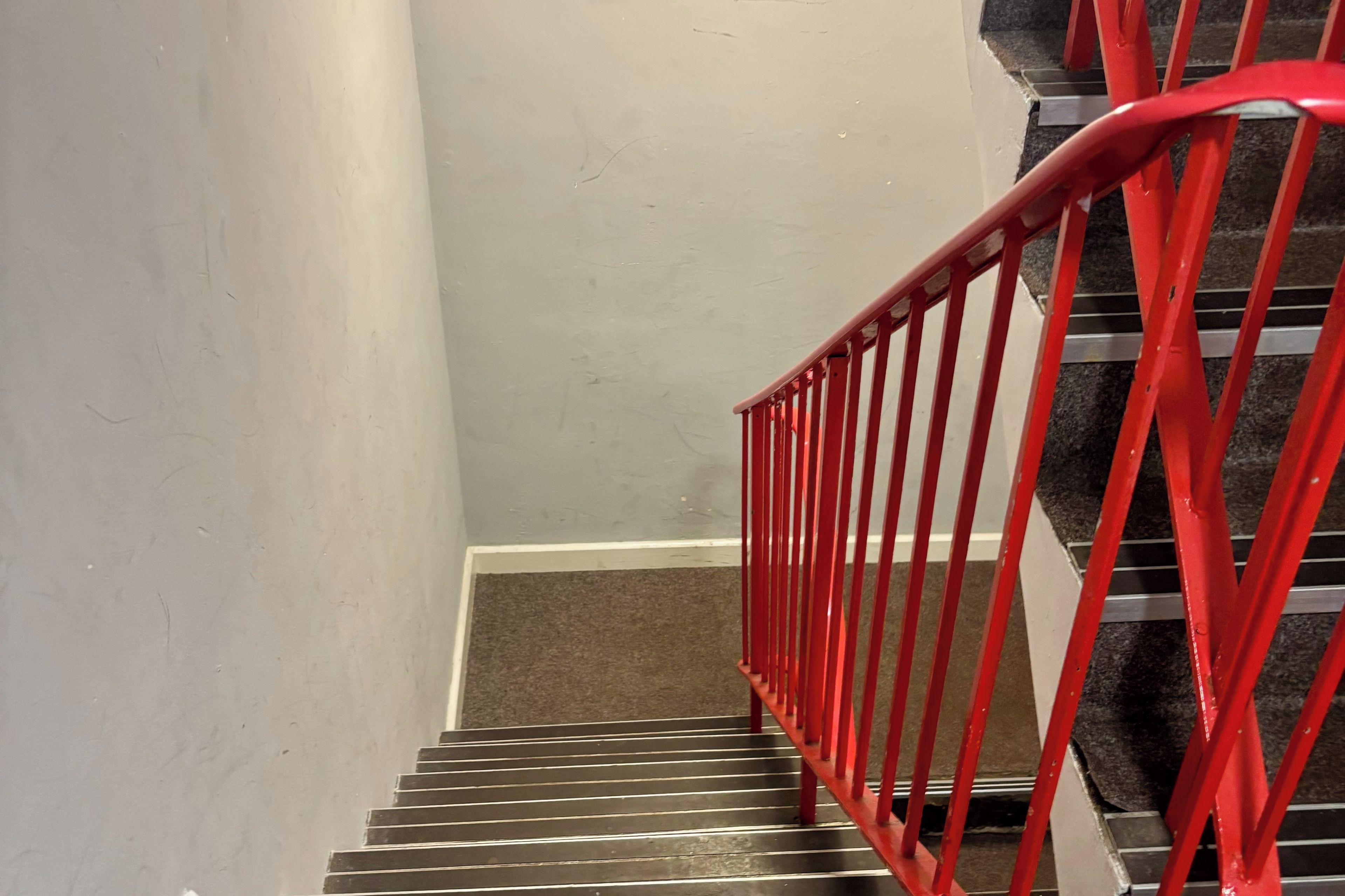 A staircase with a red handrail and a carpeted landing.