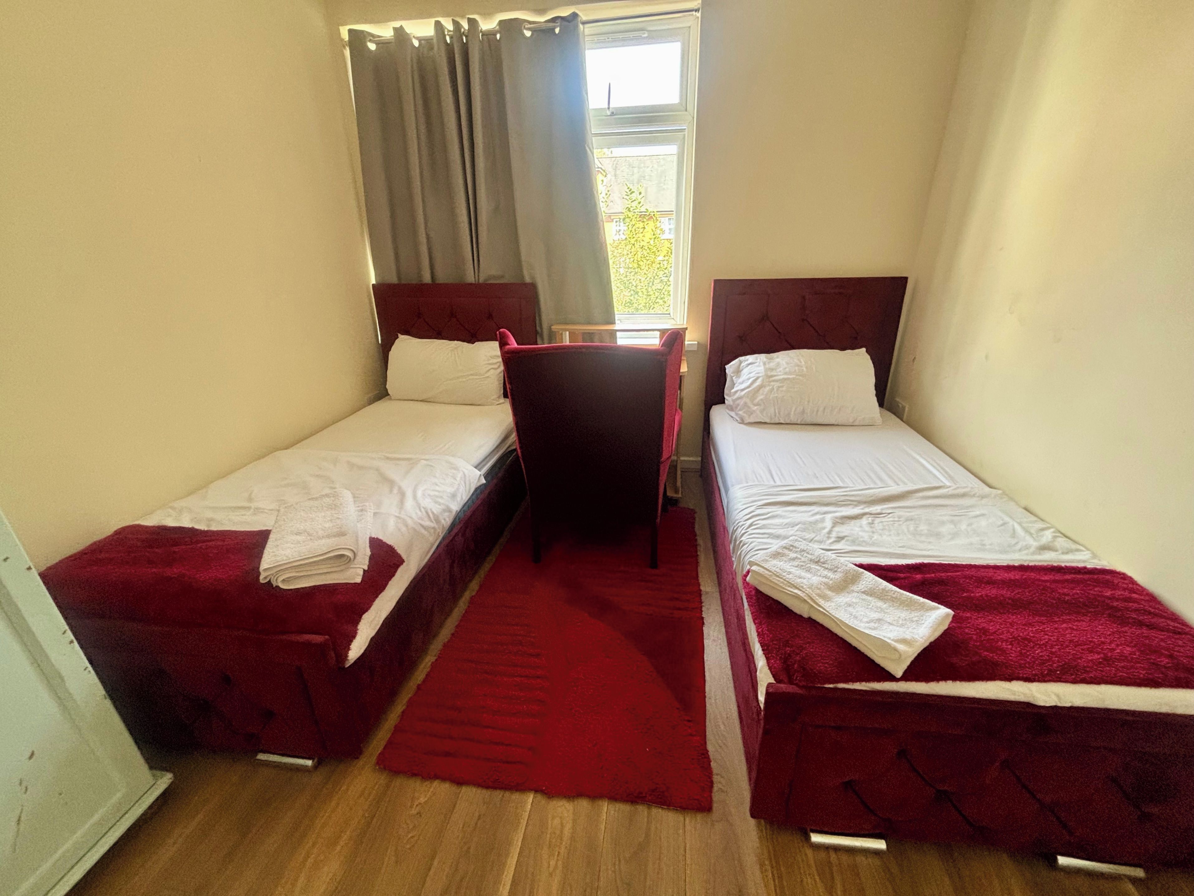 Ein kleines, gemütliches Zimmer mit zwei Einzelbetten, Holzboden und einem Fenster mit Vorhängen.