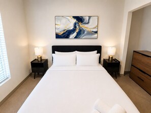 A hotel room with a large bed, two bedside tables with lamps, a wooden dresser, and a wall-mounted abstract painting. - Chic 2BR Near UAB & Dining 86 (Birmingham)