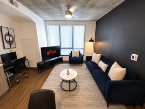 A modern living room with a dark blue sofa, a coffee table, a TV, and a ceiling fan. - Chic 2BR Near UAB & Dining 86 (Birmingham)
