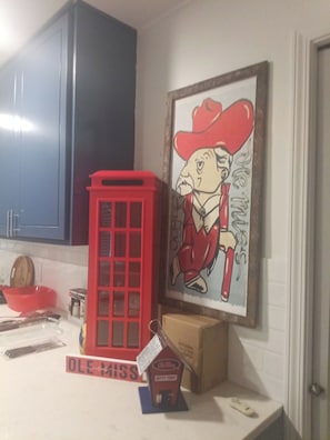 A kitchen with a red telephone booth, a framed cartoon character, and a sign that reads 'OLE MISS'. - Updated 1-bedroom condo, less than a mile from Stadium, LG covered outdoor space (Oxford)