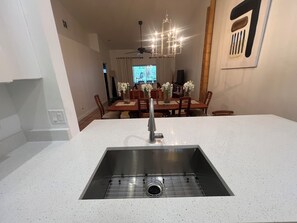 A kitchen with a stainless steel sink, a dining area with wooden chairs and a table, and a chandelier. - 3-bedroom house in tranquil Naples with cool AC breeze (Naples)