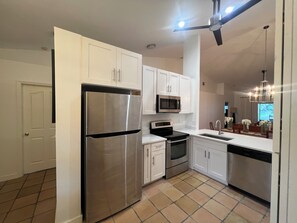 A modern kitchen with stainless steel appliances, white cabinetry, and a tiled floor. - 3-bedroom house in tranquil Naples with cool AC breeze (Naples)