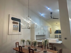 A modern dining area with a wooden table, chairs, and clear glass vases with flowers. - 3-bedroom house in tranquil Naples with cool AC breeze (Naples)
