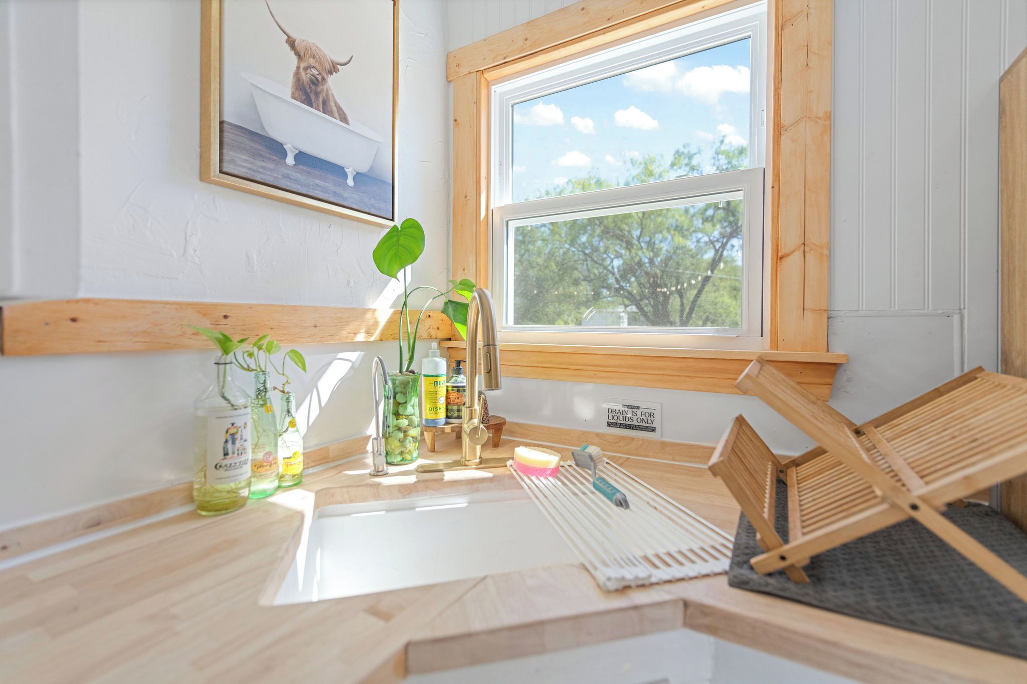 A bathroom with a wooden vanity, a sink, a window with a view of trees, and a framed picture on the wall.