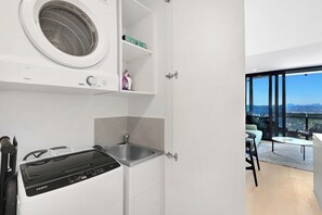 A modern kitchen with a built-in washer, a sink, and a view of the city through large windows. - Charming Water View 1BR | Steps to Casino and Tram (Broadbeach)