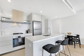 A modern kitchen with a built-in oven, a stainless steel refrigerator, and a marble countertop. - Charming Water View 1BR | Steps to Casino and Tram (Broadbeach)