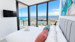 A bedroom with a large bed, a flat-screen TV, and a city view through floor-to-ceiling windows. - Charming Water View 1BR | Steps to Casino and Tram (Broadbeach)