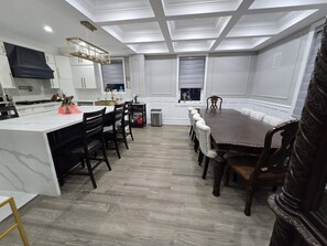 A modern kitchen with white cabinetry, a central island, and a dining area with a large table and chairs. - Country Farmhouse Retreat with Pool (Uxbridge)