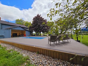 Ein Garten mit Schwimmbad, Sitzgelegenheiten im Freien, Grillplatz und einem großen Baum.