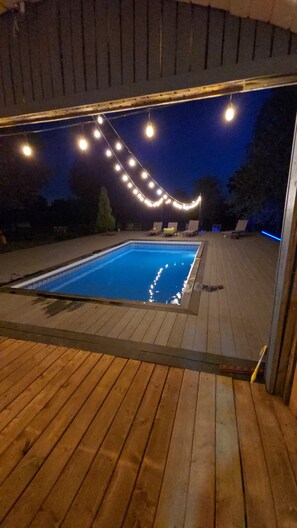 Ein Pool im Freien mit Holzterrasse, umgeben von Lichterketten.