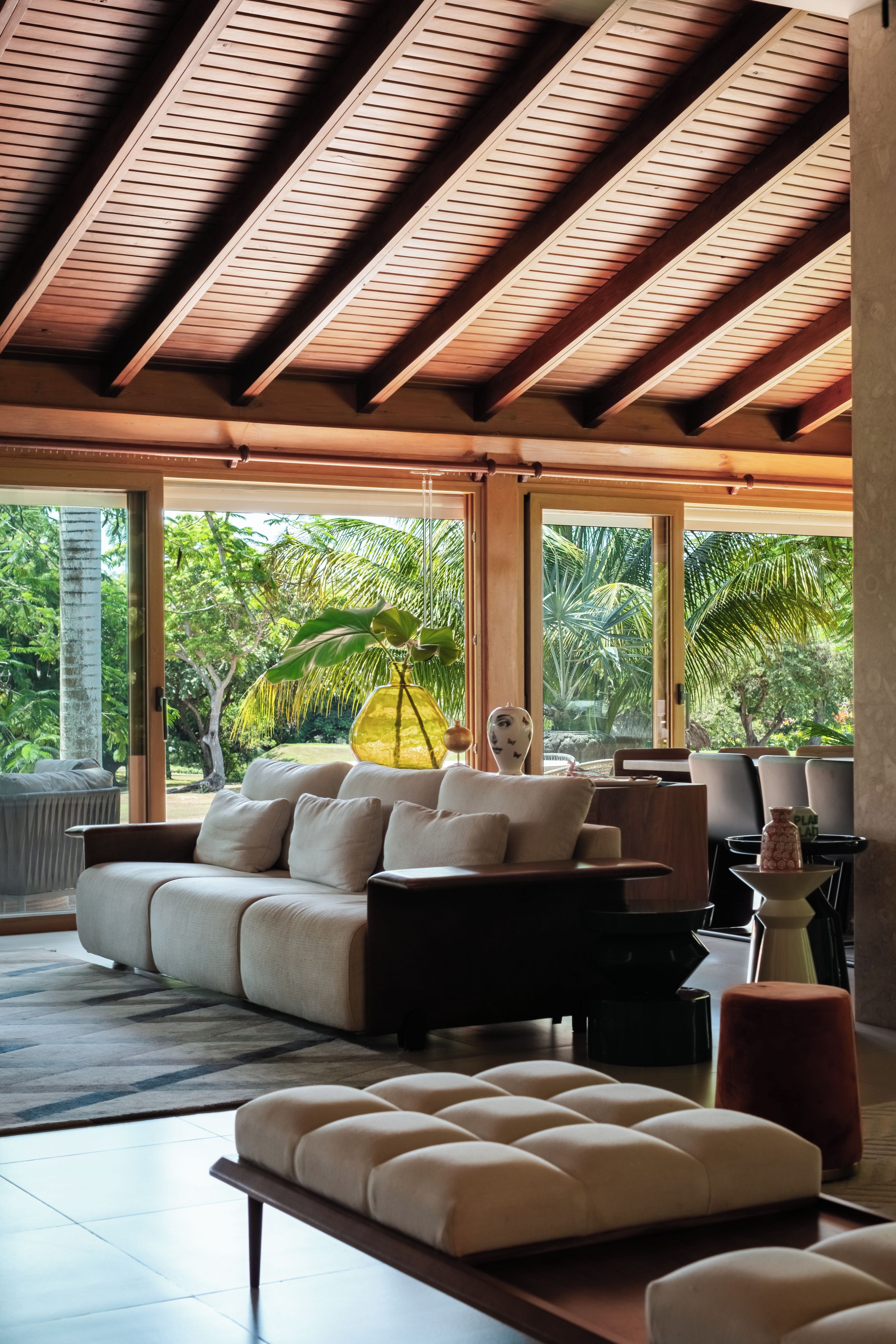 A spacious living area with a large window, a sofa, a coffee table, and a wooden ceiling structure.