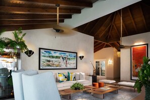 A modern living room with a high ceiling, a large painting, and a dining area with a glass wall. - Casa de Campo Golf View Villa (La romana)