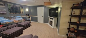 Ein Wohnzimmer mit Fernseher, Kamin, einer Couch und einer Wand mit gerahmten Bildern.