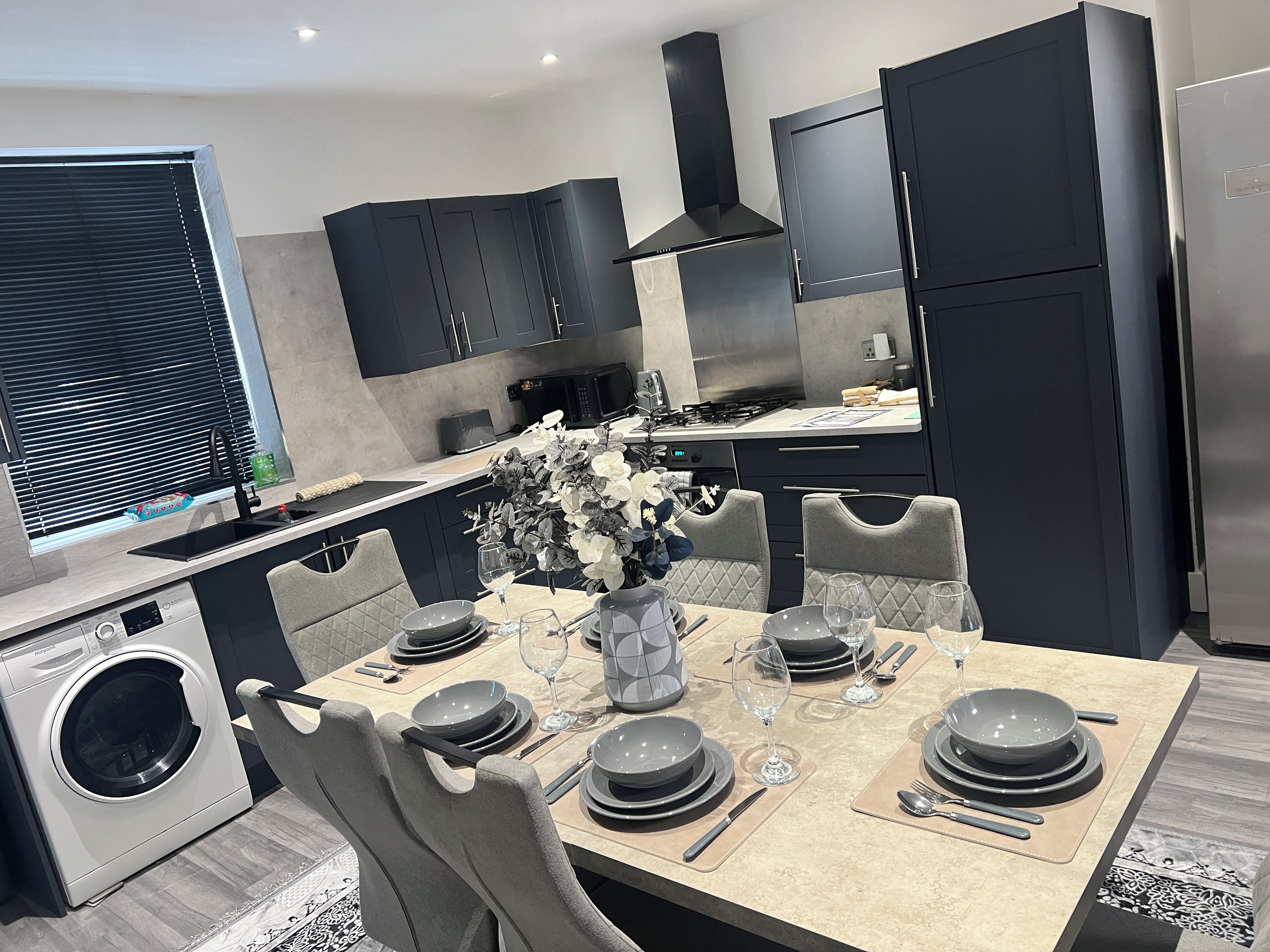 A modern kitchen with dark cabinetry, a central island with seating, and a built-in washing machine.