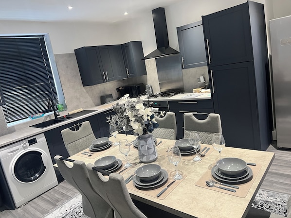 Cocina moderna con muebles oscuros, una isla central con asientos y lavadora integrada.