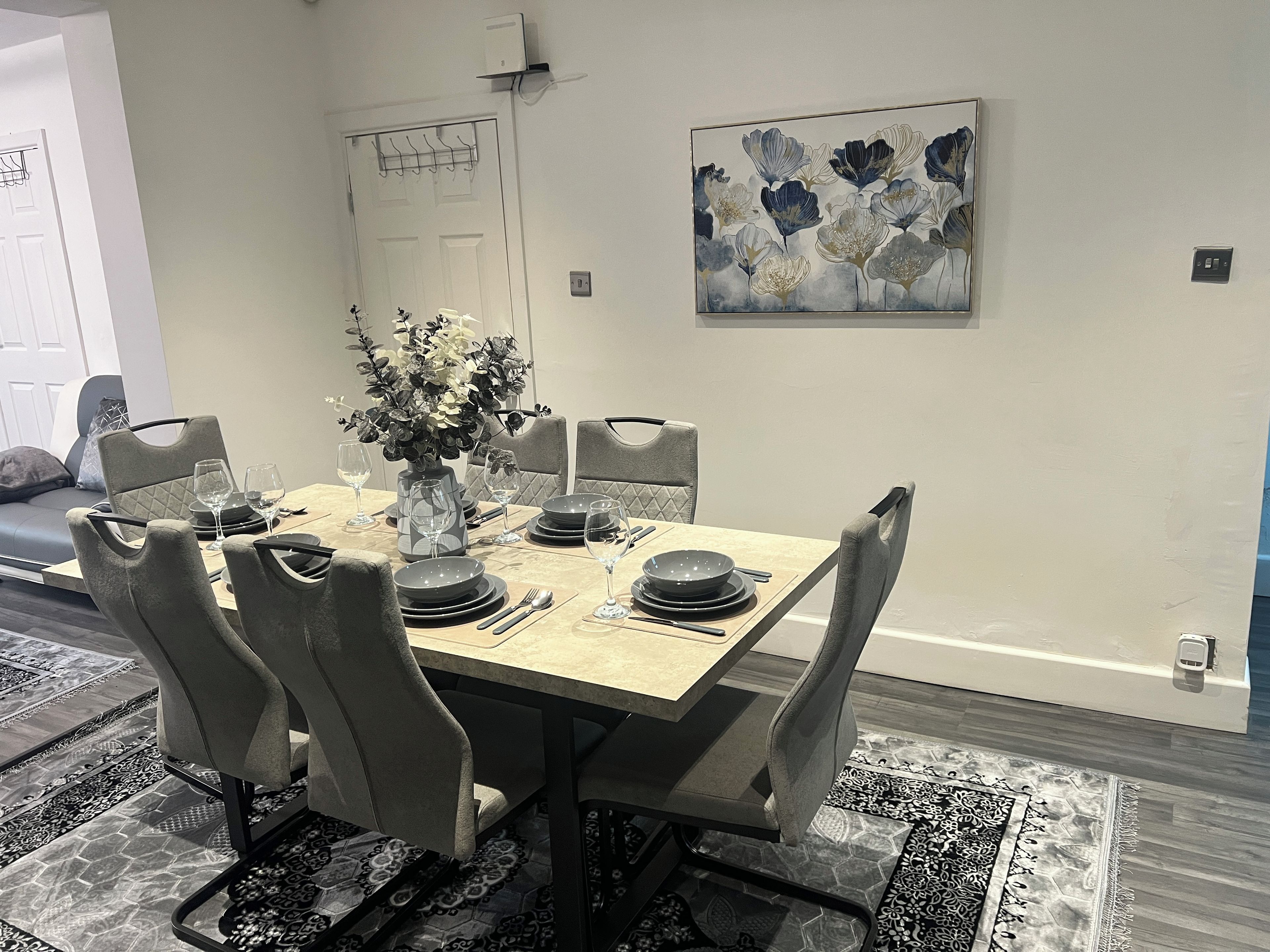 A dining area with a table set for six, chairs, a vase with flowers, and a painting on the wall.