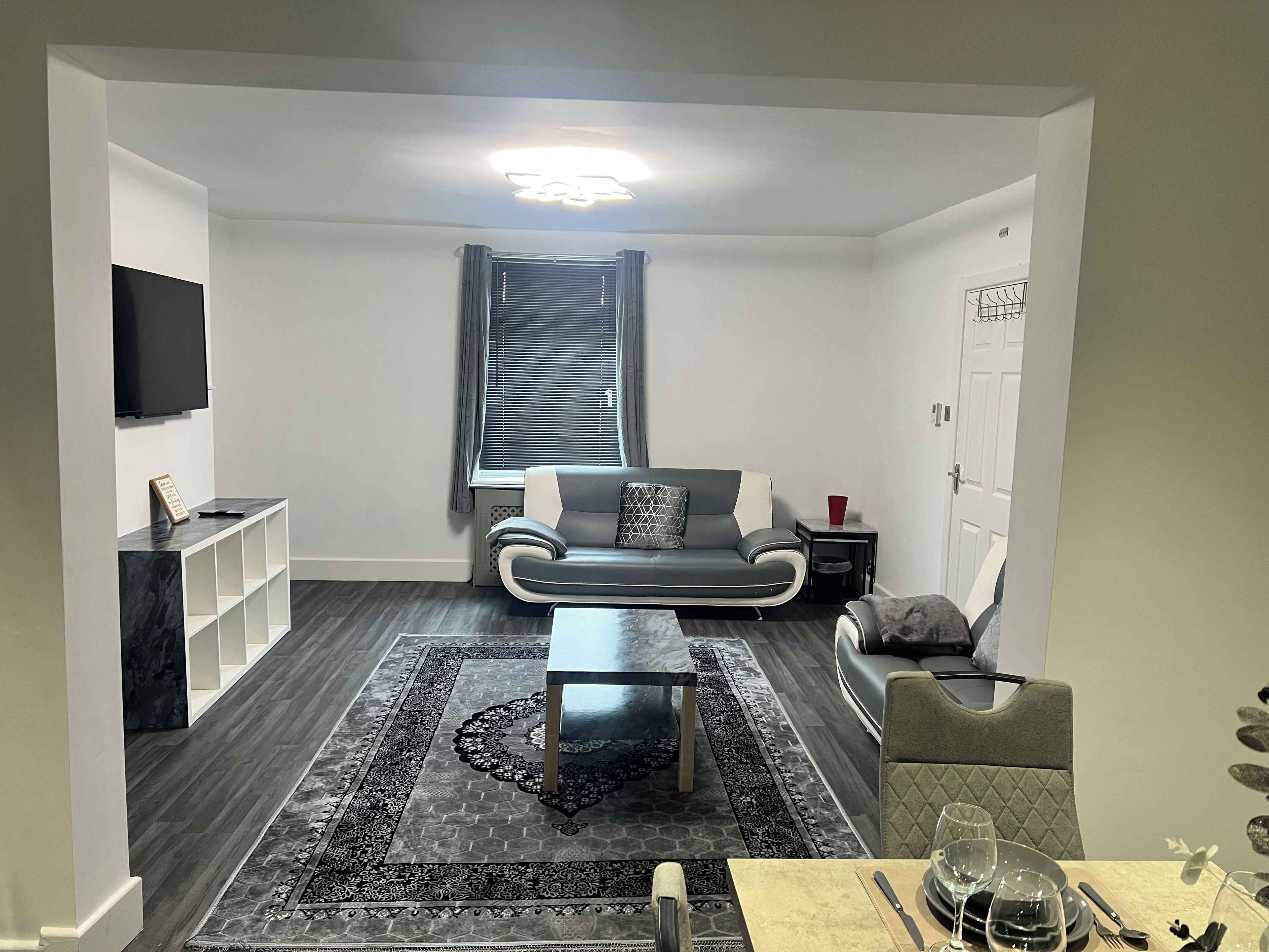 Una sala de estar moderna con un sofá, una mesa de centro, un televisor montado en la pared y un comedor con una mesa dispuesta para dos personas.