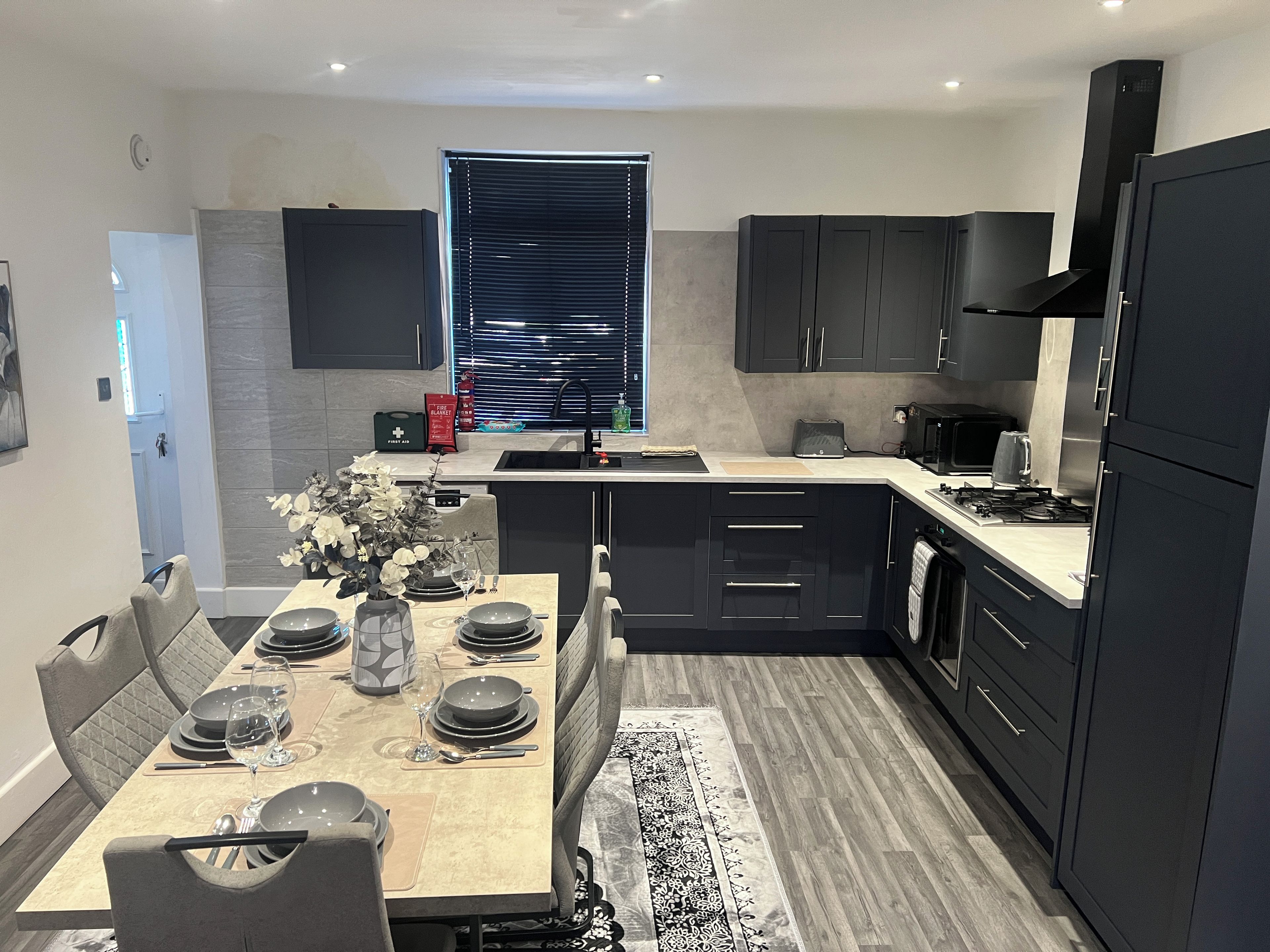 A modern kitchen with dark cabinetry, a central island, and a dining area set for four.