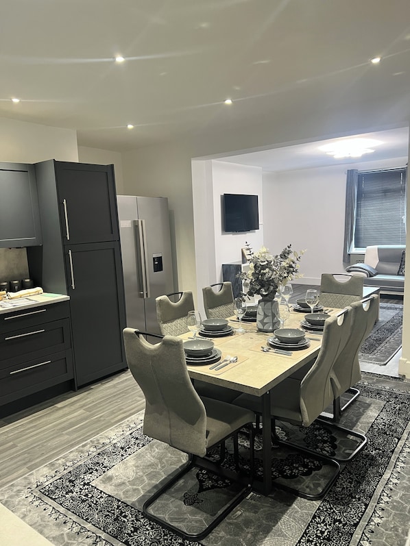 A modern dining area with a rectangular table set for four, surrounded by cushioned chairs.