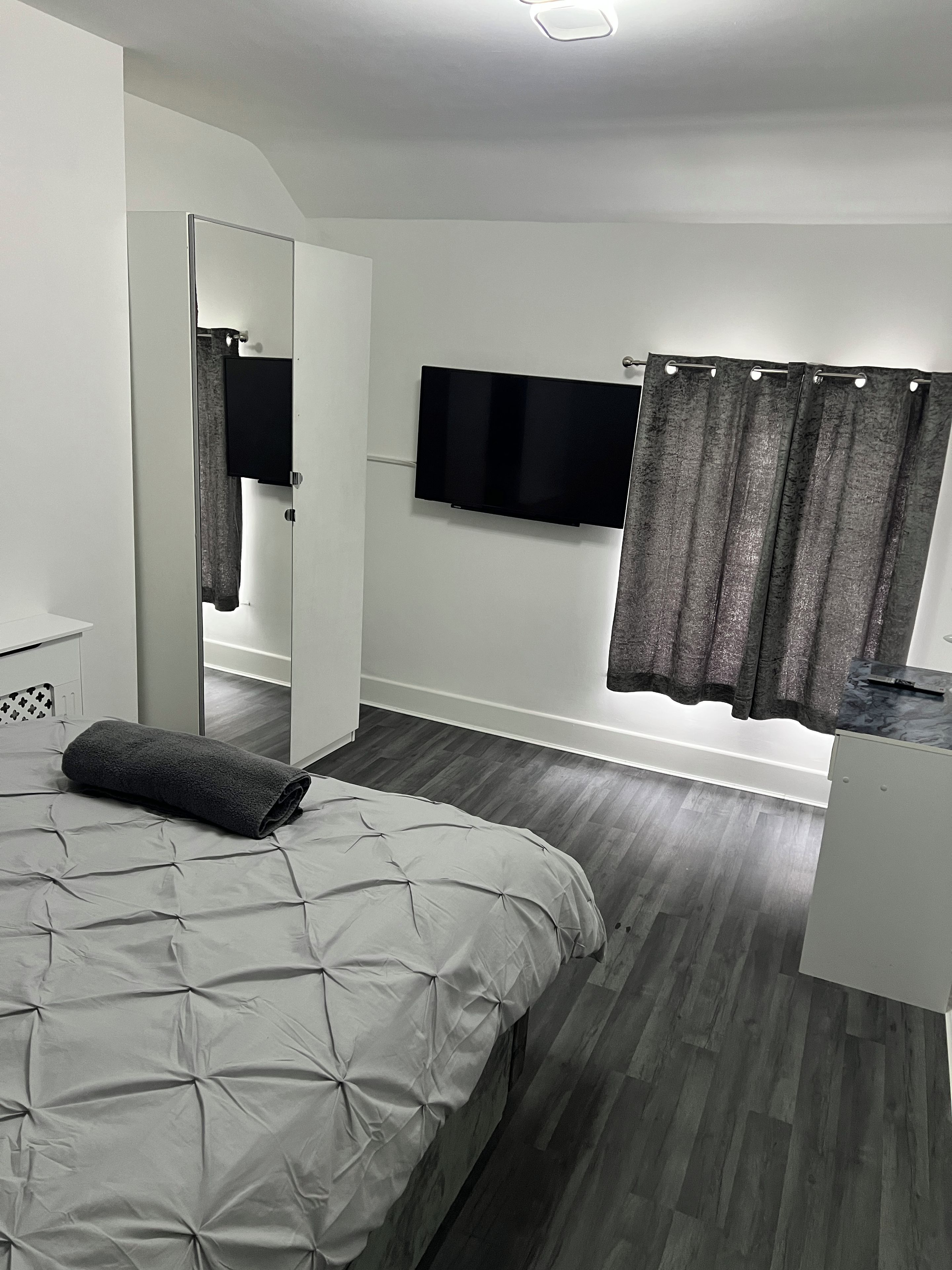 Un dormitorio con cama, televisor, espejo y ventana con cortinas.
