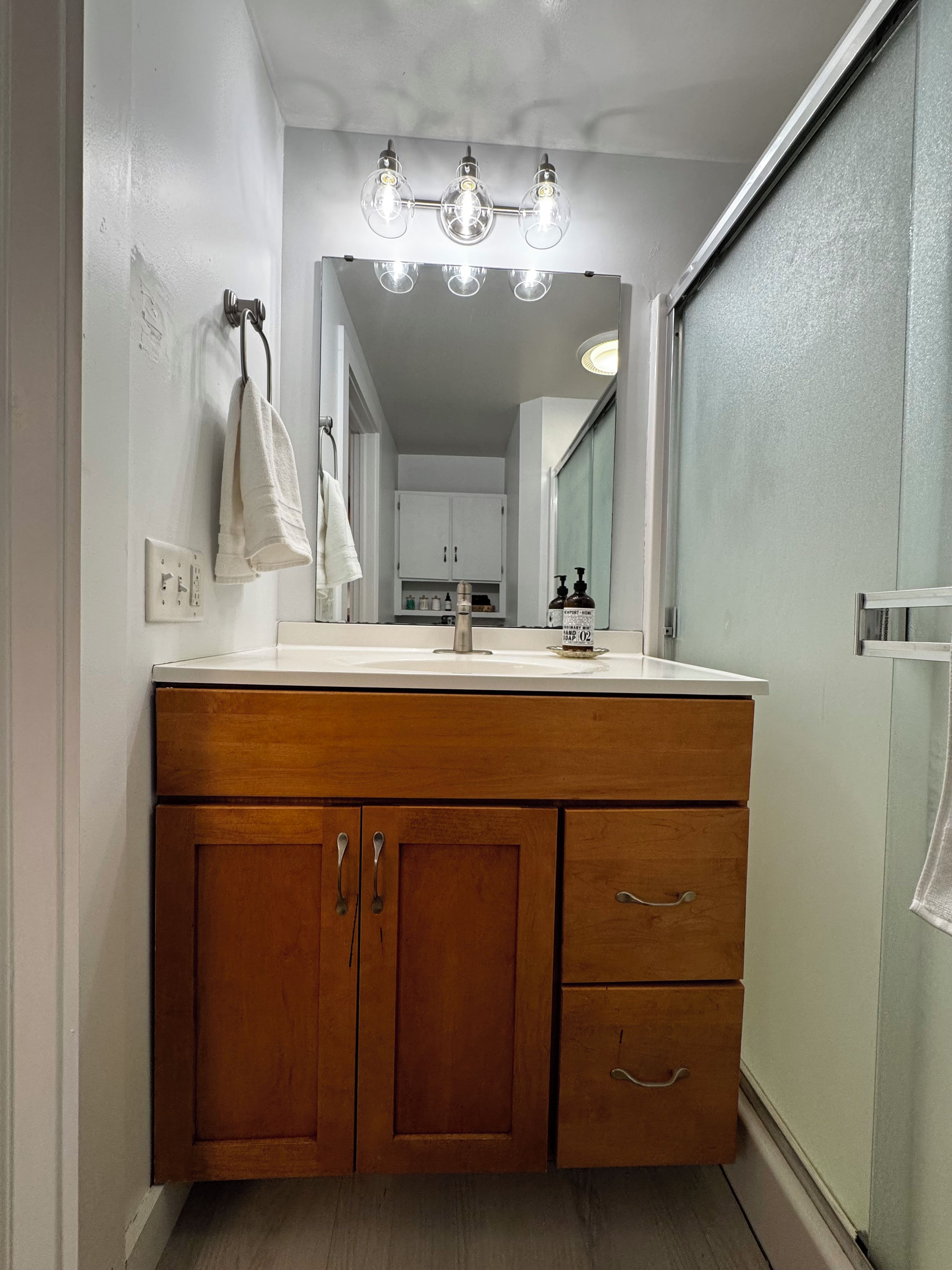 A bathroom with a wooden vanity, a mirror, and a light fixture above the mirror.