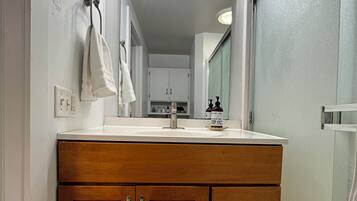 A bathroom with a wooden vanity, a mirror, and a light fixture above the mirror.