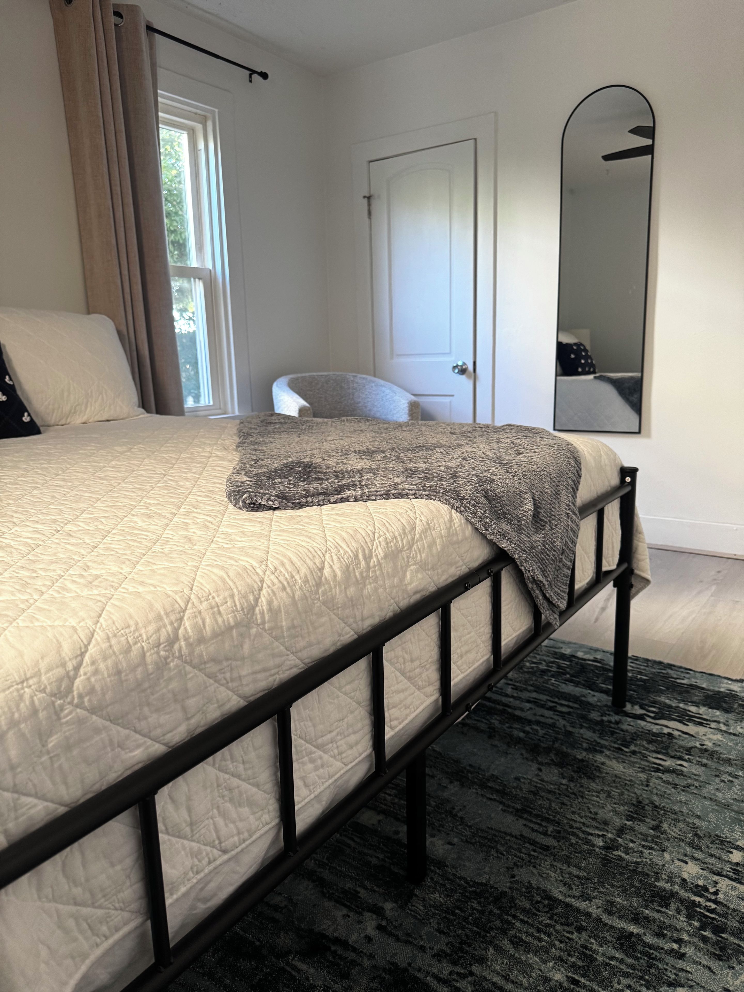 A bedroom with a bed, a door, a mirror, and a window.