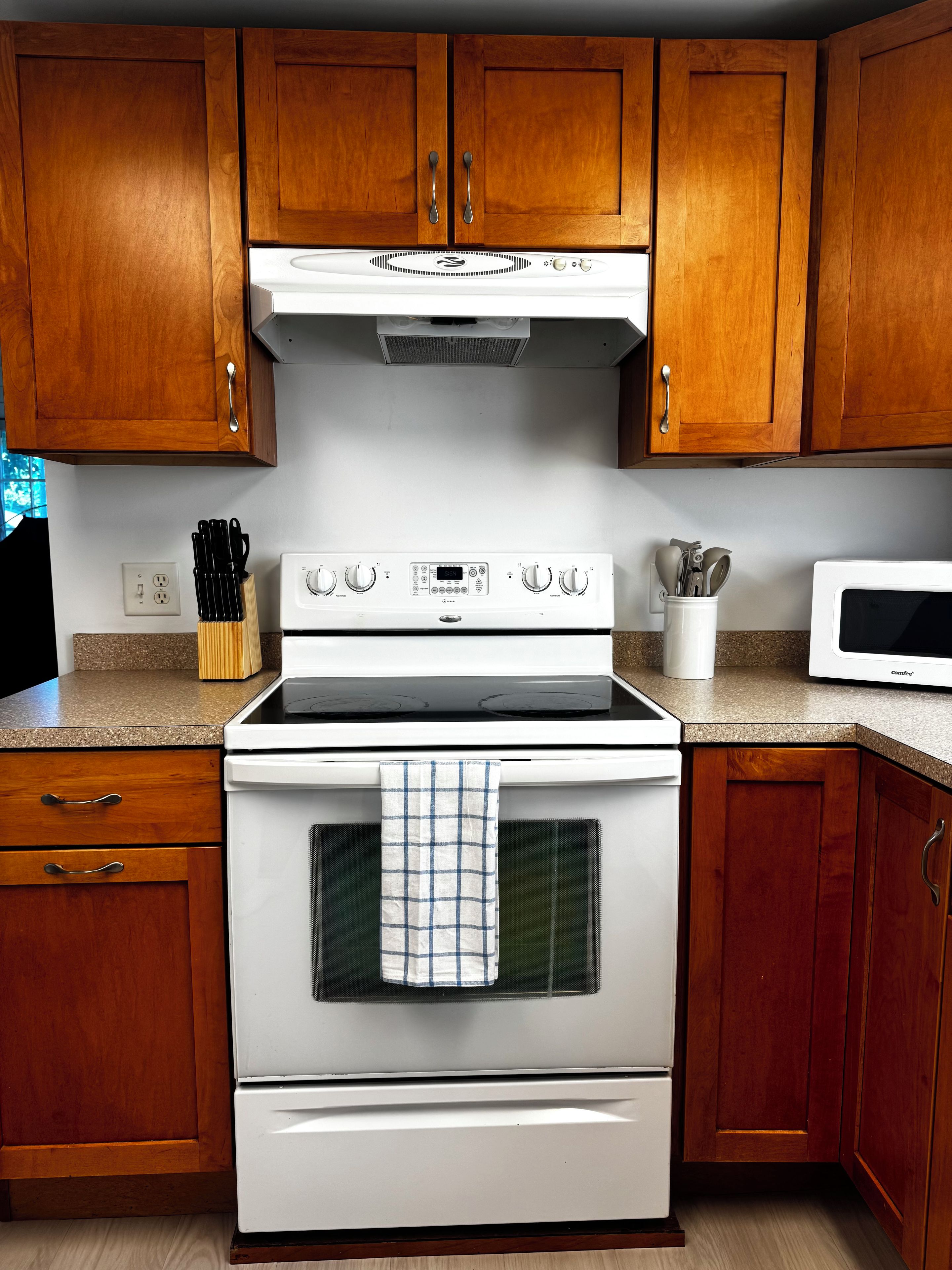 A kitchen with wooden cabinets, a stove, a microwave, and a set of knives on the counter.