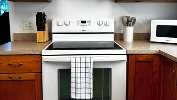 A kitchen with wooden cabinets, a stove, a microwave, and a set of knives on the counter.