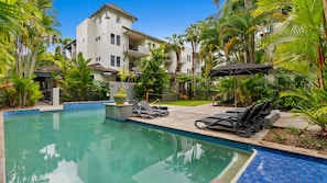 A pool with lounge chairs, a building with balconies, and tropical plants. - Ground-Floor One-Bedroom Port Douglas Stay with Shared Pool (Port Douglas)
