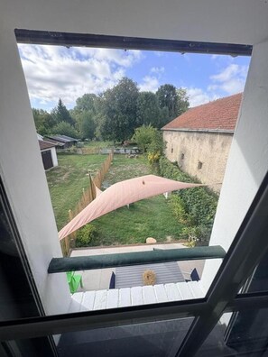 A view from a window with a clear sky, a grassy yard, a wooden fence, and a building with a red roof. - THE KEYS TO THE EMERALD (BERGNICOURT)