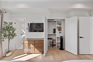 A modern living room with a wooden cabinet, a flat-screen TV mounted on the wall, and a potted plant. - Austin Escape w/ Private Patio Near Lady Bird Lake (Austin)