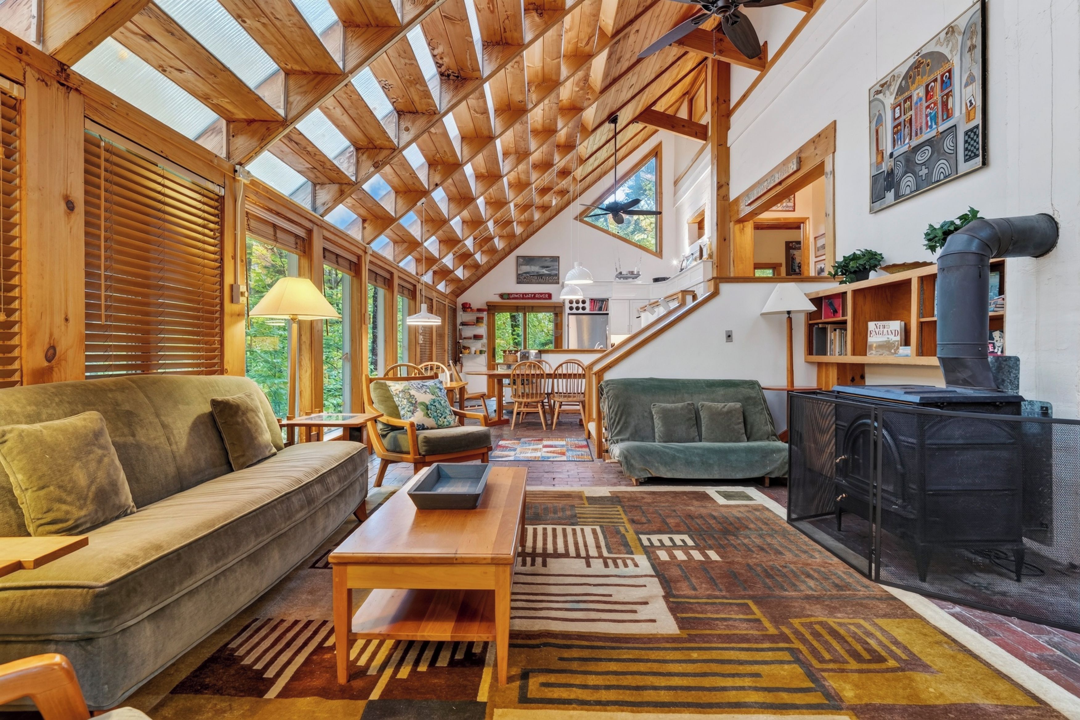 Amplia sala de estar con techo alto, vigas de madera, chimenea y vistas al exterior.