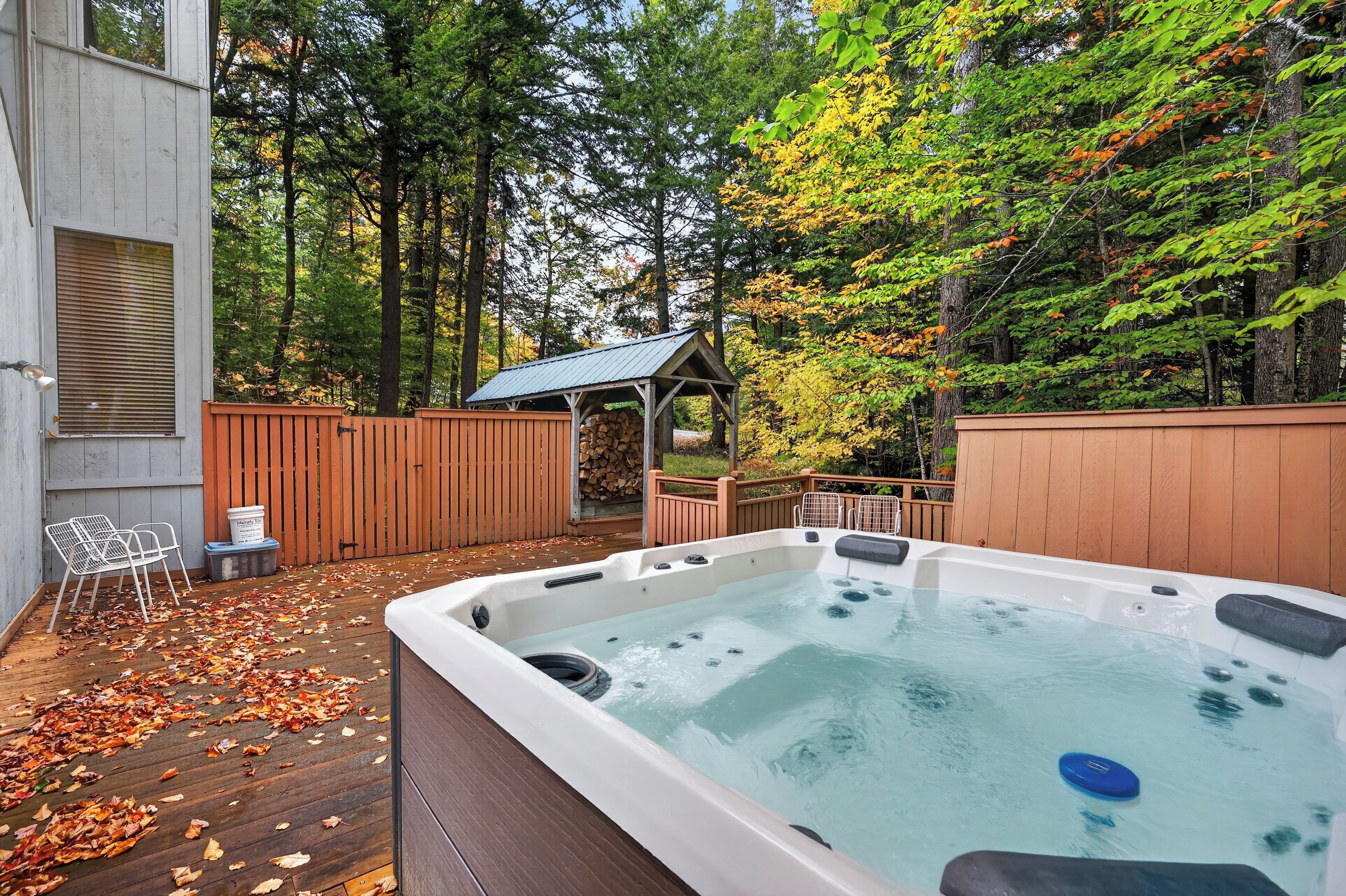 A hot tub in a backyard with a wooden deck, a wooden fence, and trees.