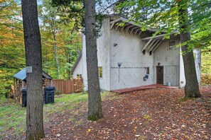 Eine rustikale Holzhütte mit Veranda und einer kleinen Werkstatt in bewaldeter Landschaft.