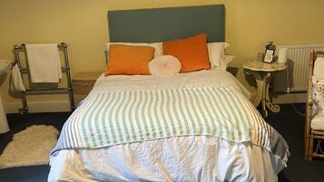 A bed with striped bedding, a headboard, and two pillows. There is a small round table with a picture frame and a lamp.