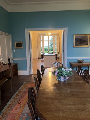A dining room with a large wooden table, chairs, a vase of flowers, and a view through a doorway to a kitchen area.