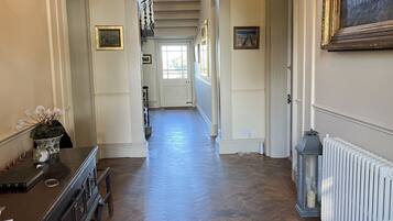 A hallway with a wooden floor, a chandelier, a deer head decoration, a radiator, and framed pictures on the walls.
