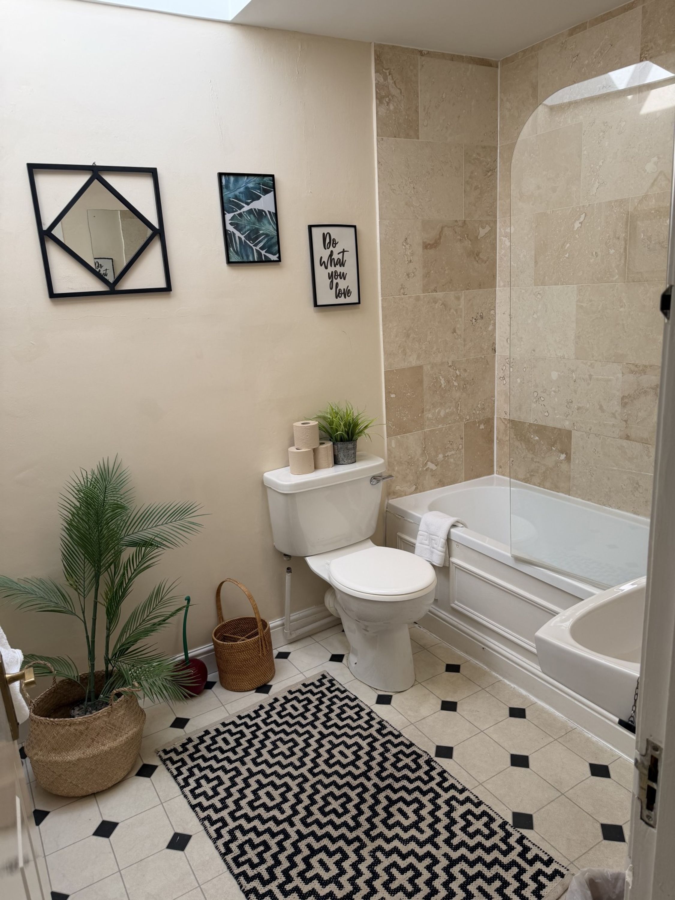 Une salle de bain comprenant des toilettes, un bidet, une baignoire et une douche. Les murs sont ornés de tableaux encadrés et il y a une plante en pot.