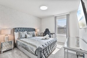 A modern bedroom with a tufted headboard, a glass desk, and a large window with blinds. - 5BR/5.5BA Clermont Home w/ Resort Pool & Golf (Clermont)