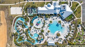 Vista aérea de um resort com várias piscinas, um edifício imponente com design de telhado singular e áreas ajardinadas.